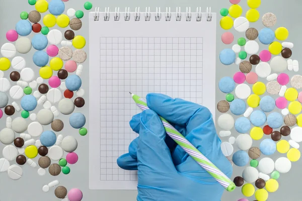 Доктор або фармацевт пише в блокноті на тлі різнокольорових таблеток — стокове фото