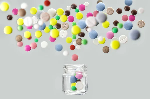 Многоцветные медицинские таблетки вылетают из стеклянной банки — стоковое фото