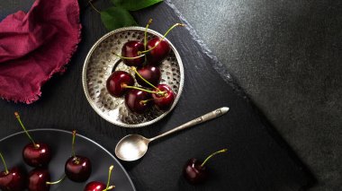 Siyah arka planda metal bir plaka içinde olgun kirazlar. Üst görünüm