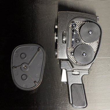 Açık kapaklı ve siyah arkaplanlı eski amatör film kamerası.