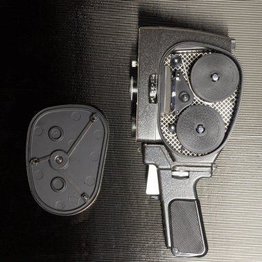 Açık kapaklı ve siyah arkaplanlı eski amatör film kamerası.