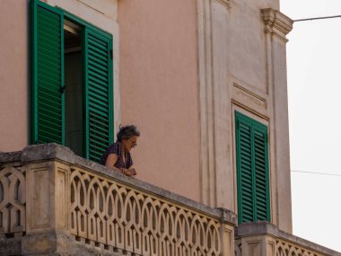 Locorotondo, İtalya - 8 Ağustos 2021: Yaşlı kadın eski kasabanın penceresinden aşağı bakıyor.
