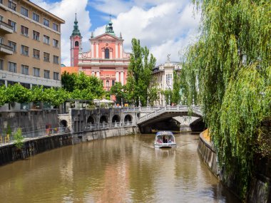 Ljubljana, Slovenya - 7 Temmuz 2025: Arka planda Fransisken Annunciation Kilisesi ile Ljubljanica Nehri manzarası.