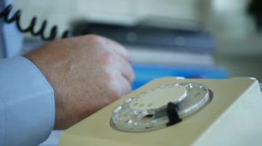 Ofis odasında eski bir iletişim teknolojisini kullanarak ayakta duran ve telefonla konuşan bir iş adamı resmi