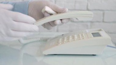 Ellerinde koruma eldivenleri olan bir adam telefonu temizliyor ve dezenfekte ediyor. Sprey ve ıslak mendil kullanıyor.