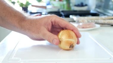 Mutfakta bir adam salata için beyaz soğan doğruyor.