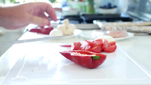 Muž v kuchyni krájení lahodné čerstvé červené papričky v plátcích na salát — Stock video