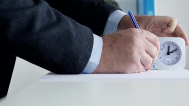 Homme d'affaires vérifie l'horloge de bureau et complète avec un stylo un test pour un examen — Video