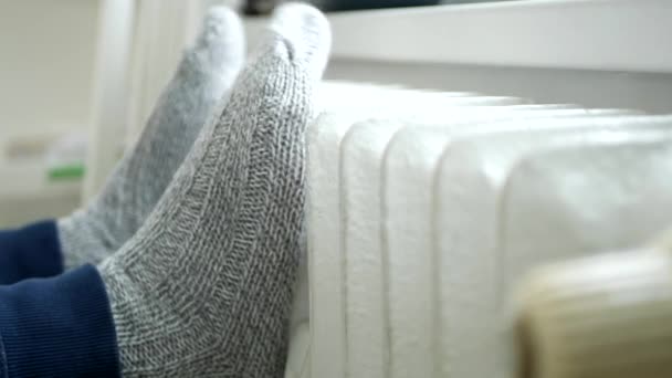 Расслабленный человек сидит и согревается ногами в вязаных шерстяных носках на нагревательном радиаторе — стоковое видео