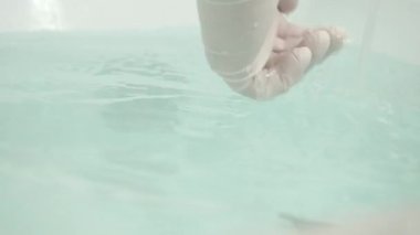 Ellerinde koruyucu eldivenleri olan hemşire tıbbi terapi için sıcak bir banyo hazırlıyor.