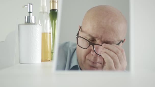 Mężczyzna w okularach siedzi przed lustrem w łazience i myśli rozczarowany — Wideo stockowe