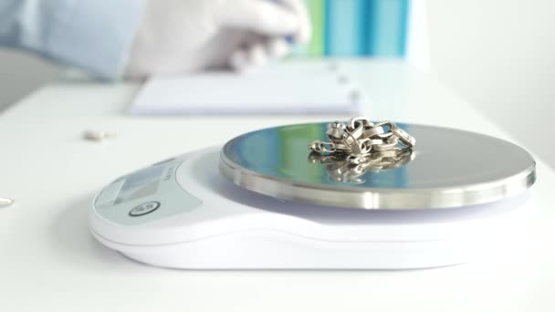 Jeweler in a Jewelry Store Weighs a Gold Bracelet Using an Electronic Scale and Notes in a Table in Blurr — Stock Video