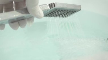 Ellerinde koruyucu eldiven olan hemşire duş başlığını kullanarak sıcak bir banyo hazırlıyor.