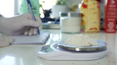 Mutfaktaki Şef Elektronik Ölçek kullanarak ve Yemek Pişirme Tarifi Yazarak Beyaz Un Tartı Alıyor