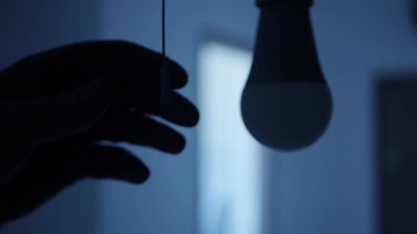 Eine Person zieht das Schaltkabel und schaltet die Glühbirne in einem dunklen Raum ein. LED-Licht im Büroraum einschalten. — Stockvideo