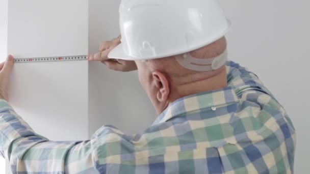 Mann trägt weißen Helm Verwenden Sie ein Klebeband Maß und nehmen Sie die Wand Dimension in einem Apartment-Zimmer — Stockvideo
