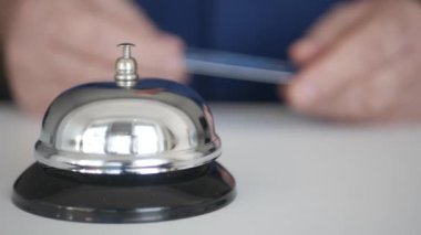 Otel resepsiyonunda elinde kredi kartı olan bir turist Ödeme için resepsiyonisti çağıran çan butonuna basıyor.