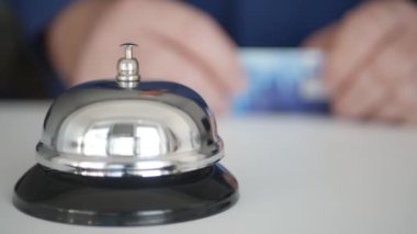 Otel resepsiyonunda elinde kredi kartı olan bir turist Ödeme için resepsiyonisti çağıran çan butonuna basıyor.