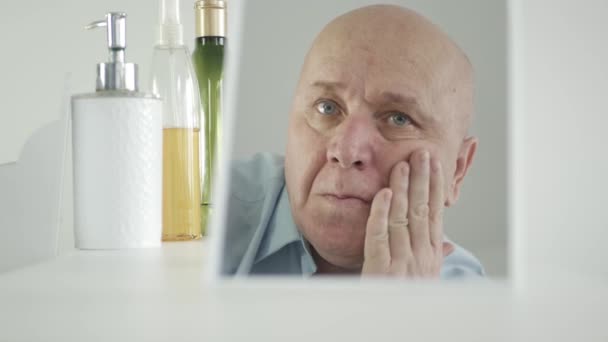 Mężczyzna patrzy w lustro łazienki i pociera twarz kremem nawilżającym skórę — Wideo stockowe