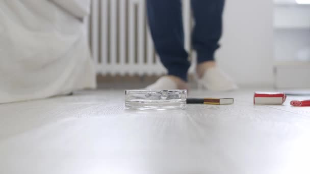 Dospělá osoba na domácí procházky v ložnici s pantoflemi, Polož na podlahu zapálenou cigaretu a sklenici s alkoholem. — Stock video
