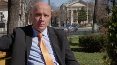 Businessman Sitting on a Bench in Downtown Park, Smiling Confidently, Waiting for a Meeting.