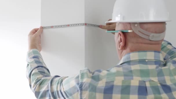 Ingeniero que trabaja en un sitio de construcción, usando una cinta métrica para comprobar las dimensiones de la pared en una habitación. — Vídeo de stock