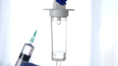 Medical Perfusion Dripping and a Doctor in Blurred in Background with a Syringe with Vaccine in Hand. Slow Motion Shooting.