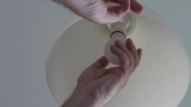 Electrician's Hand Changing a Led Bulb in a Lamp and Turning On the Light in the Room.