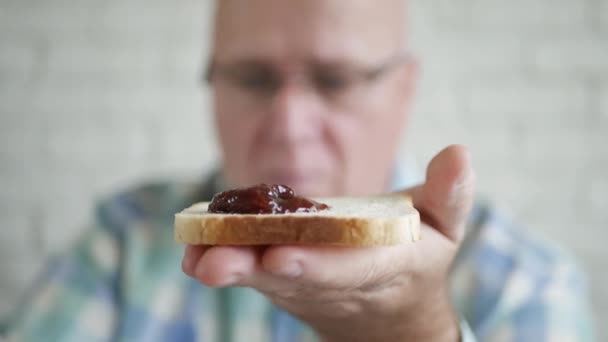 Älterer Mann legt morgens süße und aromatische Fruchtmarmelade auf ein Stück Brot zum Frühstück. — Stockvideo