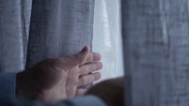 Perdenin Arkasından casusluk yaparak perdeleri kaldırır ve pencereye bakar. Pencere Perdesinden Dışarıya Bakan Bir Kişi.