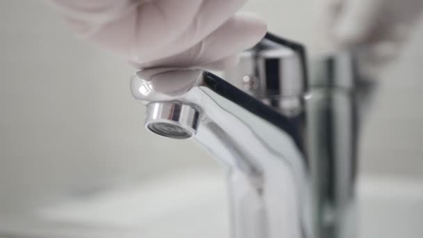 Ellerinde koruyucu eldivenler olan tıbbi kişi banyoda lavabo musluğunu açıyor.. — Stok video