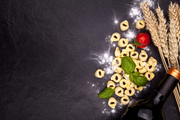 Tortellini e farina su un piatto di pietra nera . Immagine Stock