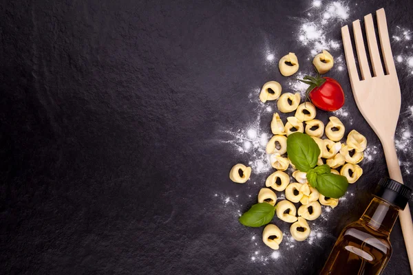 Tortellini e farina su un piatto di pietra nera . Fotografia Stock