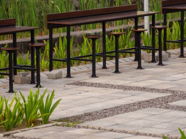 Ahşap masaları ve uzun sanayi sandalyeleri olan güzel ve basit bir açık hava oturma alanı. Sert çimento cepheli açık hava kafesi için dikim dekorasyonu.