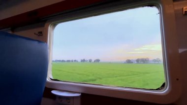 Tren penceresinden bak. Şehirlerarası bir trenin penceresinden güzel bir manzara, yeşil pirinç tarlaları ve kenarlar boyunca uzanan yerleşim alanları..