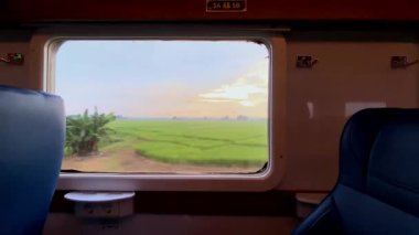 Tren penceresinden bak. Şehirlerarası bir trenin penceresinden güzel bir manzara, yeşil pirinç tarlaları ve kenarlar boyunca uzanan yerleşim alanları..