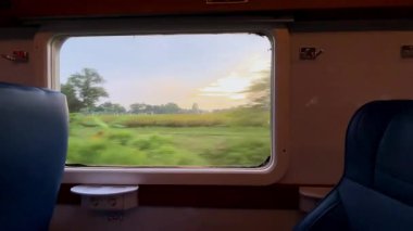 Tren penceresinden bak. Şehirlerarası bir trenin penceresinden güzel bir manzara, yeşil pirinç tarlaları ve kenarlar boyunca uzanan yerleşim alanları..
