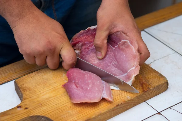 Primer plano menin la cocina está cortando cerdo en la tabla de cortar — Foto de Stock