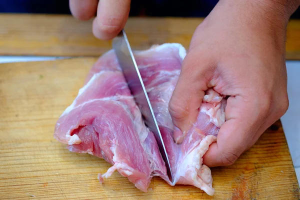 Primer plano menin la cocina está cortando cerdo en la tabla de cortar — Foto de Stock