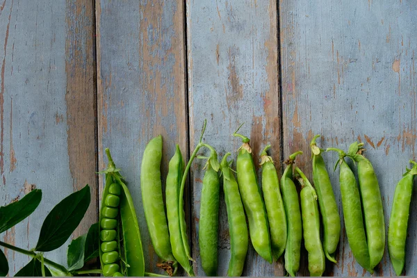 Pois verts en gousses fraîchement cueillis sur table rustique en bois — Photo