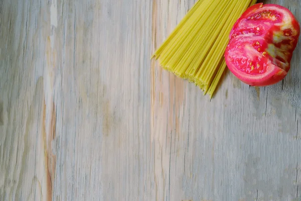 Raw spaghetti pasta and half tomato on wood background — Stock Photo, Image