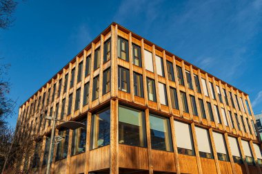 Modern wooden office building with large windows and sustainable architectural design illuminated by warm sunlight under a clear blue sky.