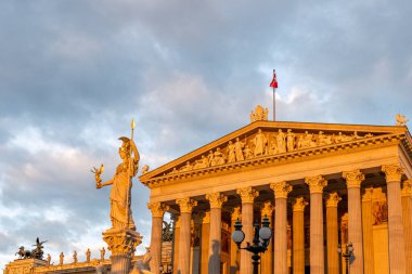 Sabah ışığı klasik bir bina ve heykeli aydınlatıyor zarif sütunlar ve detaylarla, şafak vakti yumuşak altın bir gökyüzünün altında yakalandı..