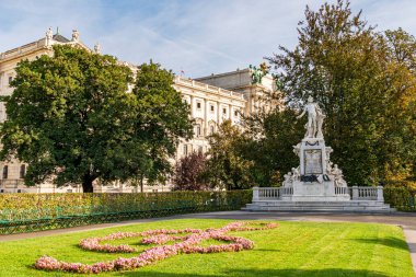 Arka planda yeşil çimenler, ağaçlar ve kültür, sanat ve mirası temsil eden tarihi mimarisi olan güneşli bir parktaki zarif mermer anıt..