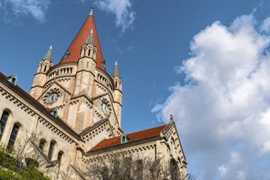 Kırmızı çatılı ve saatli tarihi kilise kulesi beyaz bulutlu açık mavi gökyüzü altında klasik Avrupa mimarisi gündüz yakalanmış..