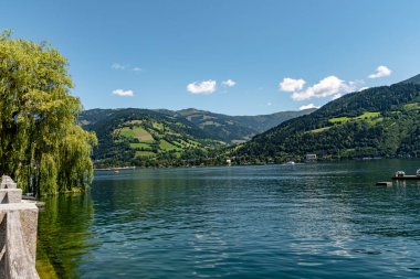 Berrak mavi gökyüzünün altında yeşil dağlarla çevrili güzel bir göl ve sakin sularda yansımaları var. Huzurlu yaz manzarası ve doğa manzarası.