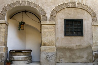 Taştan kemerleri, eski bir kuyusu ve klasik bir penceresi olan sakin kırsal avlu duvarı mimari, miras ve seyahat temaları için ideal sıcak tarihi bir atmosfer yaratıyor..