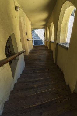 Tahta merdivenler ve taştan bir avluya uzanan sıcak kemerli duvarlarla kaplı, kırsal, tarihi ve davetkar bir mimari sahne yaratıyor..