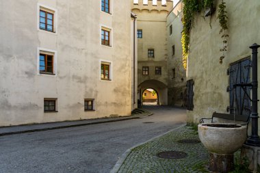 Eski taş binalar ve yumuşak gün ışığı ve kaldırım taşlarından detaylarla donatılmış kemerli bir geçitle çevrili sessiz tarihi bir ara sokak. Sahne, sakin, zamansız Avrupa şehir yaşamını ve miras yolculuğunu anımsatıyor.