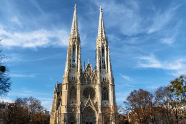 Ağaçların çerçevelediği açık mavi gökyüzüne karşı yükselen ikiz kuleleri olan Gotik bir katedralin ön görüntüsü. Avrupa 'nın görkemli mimarisi tarihi, maneviyatı ve seyahat cazibesini aktarıyor.